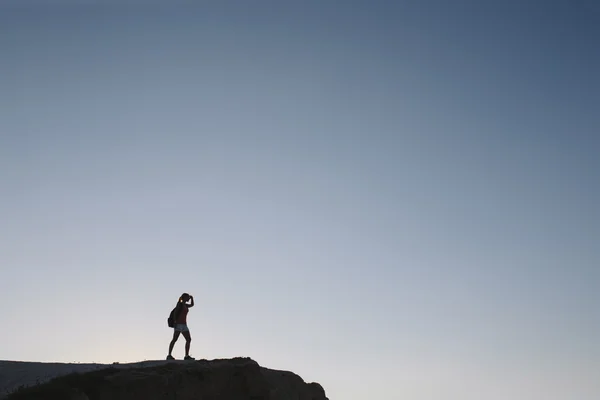 Silhouette young woman tourist with backpack standing on cliff — Stock Photo, Image