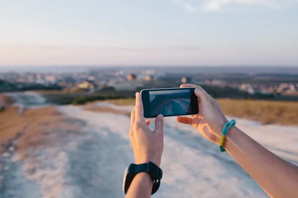 Unga kvinna händer med hjälp av en mobiltelefon för att ta foto utomhus. suddig utsikt kulle, stad och hav på en bakgrund — Stockfoto