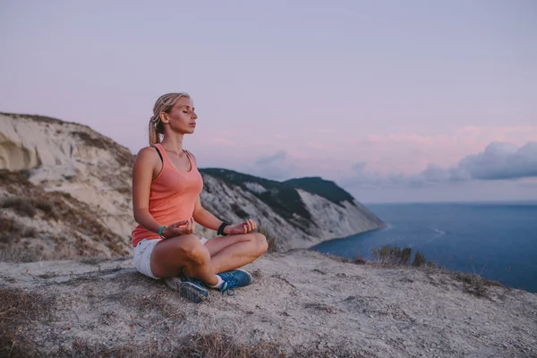 Jeune femme faisant position de lotus de yoga avec les yeux fermés en plein air sur la falaise de crête de montagne de fond et la mer. Concept de voyage style de vie sportif — Photo