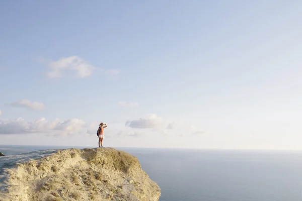Jeune femme randonneuse avec sac à dos debout sur le sommet de la montagne et regardant vers une mer. Concept de voyage style de vie sportif — Photo