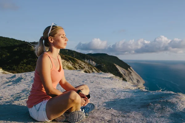 Young woman doing yoga lotus position outdoor on the background mountain peak cliff and sea. — Stock Photo, Image