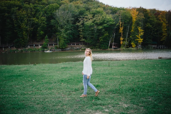 Jovem mulher em uma camisola branca e jeans azul andando ao ar livre no parque — Fotografia de Stock