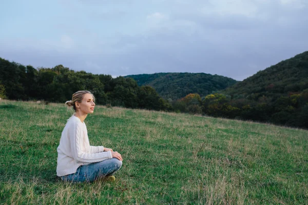 Mujer joven feliz en un suéter blanco y pantalones vaqueros azules que relajan en la hierba en un prado. mujer disfrutando de la vida al aire libre — Foto de Stock