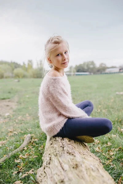 Blond tjej sitter med korsade ben på en stock utomhus — Stockfoto