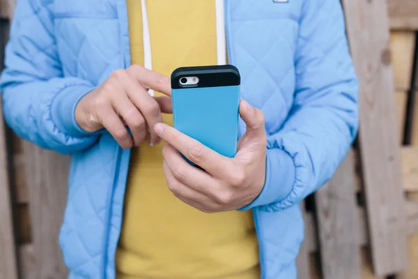 Hombre usando el teléfono inteligente sobre fondo de madera. imagen recortada de un joven enviando un mensaje de texto desde su teléfono celular — Foto de Stock