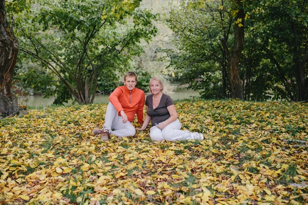 Hombre joven en un suéter rojo y una mujer anciana en el parque en el fondo del bosque de otoño y el lago. hijo y madre al aire libre — Foto de Stock