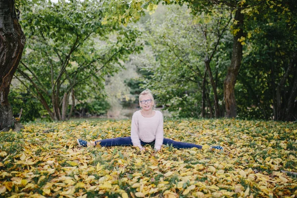 A menina senta-se no cordel em um contexto de uma floresta de outono e folhas. Menina faz exercícios esportivos ao ar livre — Fotografia de Stock