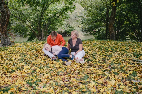 Chica, hombre joven en un suéter rojo y una mujer anciana sentada en el parque en el fondo del bosque de otoño y el lago. hija, padre y abuela se divierten al aire libre — Foto de Stock