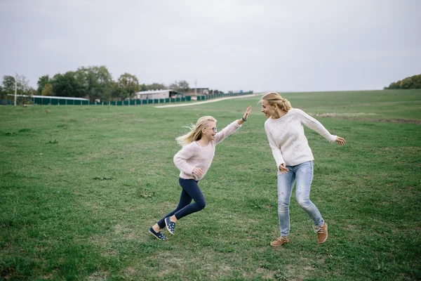 Feliz joven mujer y niña juegan en el parque. madre e hija se divierten al aire libre en el prado — Foto de Stock