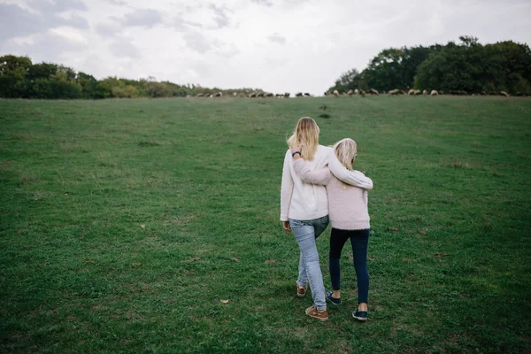 Jovem mulher e menina abraçando e andando no parque. mãe e filha ao ar livre no prado — Fotografia de Stock