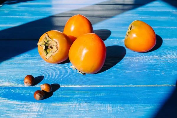Ripe persimmon on a blue wooden background, near lies group of brown hazel nut. Vegetarian nutrition.  Healthy eating, dieting — Stock Photo, Image