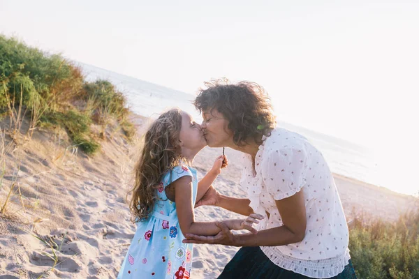 Mulher está beijando sua filha em uma praia — Fotografia de Stock