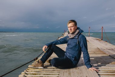 ahşap bir iskele üzerinde oturan genç adam 