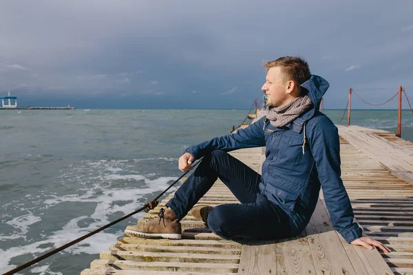 Ahşap bir iskele üzerinde oturan genç adam — Stok fotoğraf