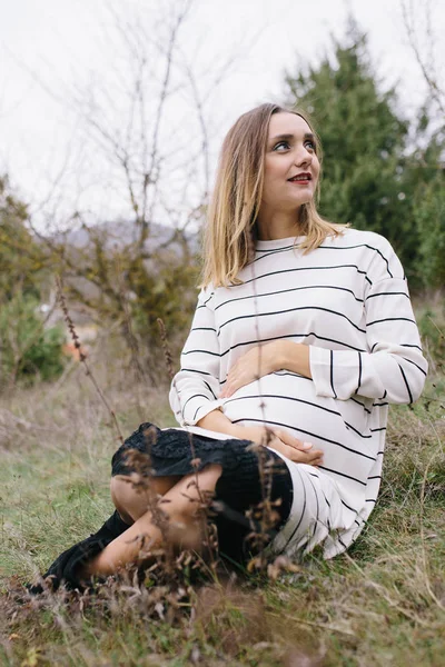 Mulher grávida está sentado na grama — Fotografia de Stock