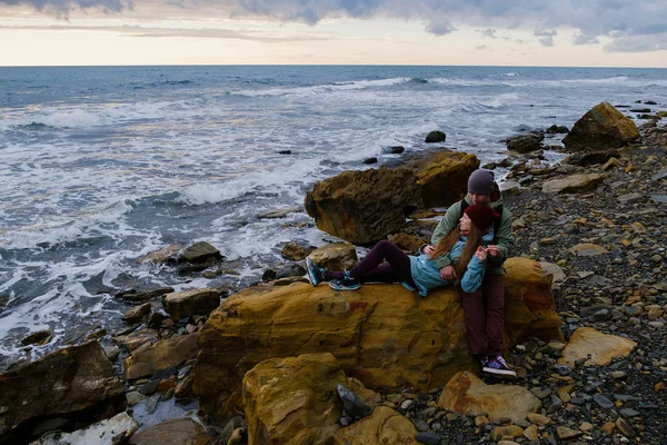 Młoda para siedzi na skałach na morzu — Zdjęcie stockowe