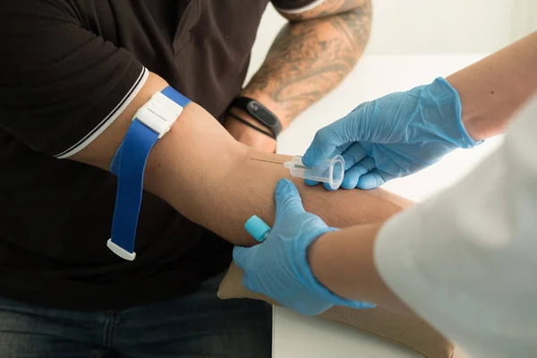 Close up nurse pricking needle syringe in the arm patient drawing blood sample for blood test. Close up