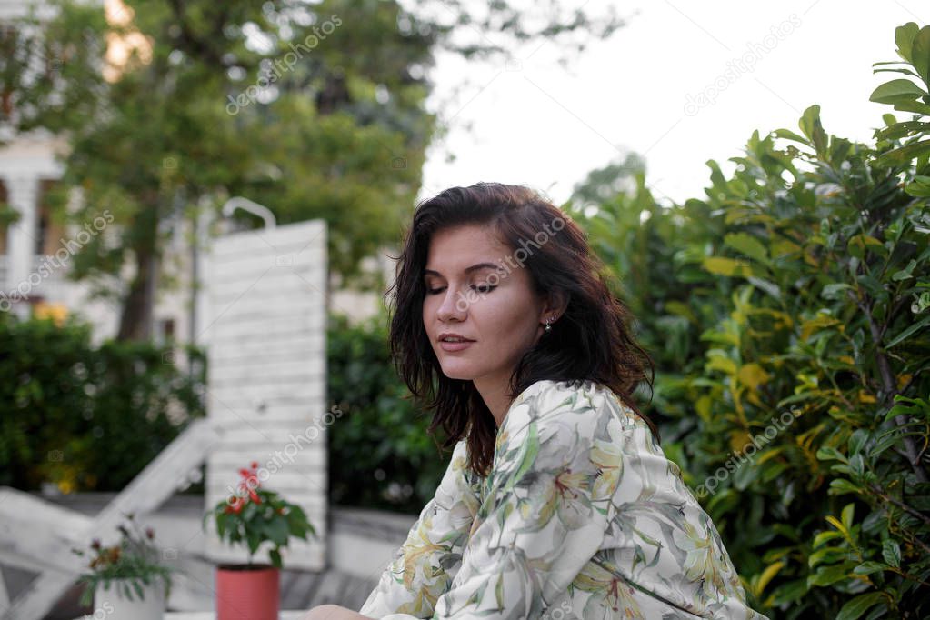 brunette young woman in floral spring summer blouse. Girl posing on patio. Summer floral outfit. Stylish wavy hairstyle. Fashion photo.