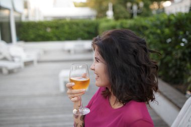 pembe gülümseyen esmer genç kadın ilkbahar yaz elbise şarap ile. Kız verandada şarap ile poz. Moda fotoğraf. 