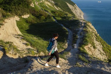 Mavi denize yakın Hills yürüyen güzel esmer kadın. Kadın turist Okyanusu yakınlarındaki tepe üzerinde sırt çantası ile. Seyahat, özgürlük ve aktif yaşam tarzı kavramı