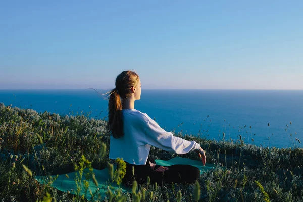 Genç kadın pratik Yoga yılında Lotus pozisyonu açık. genç kız deniz yakınlarındaki tepe üzerinde rahatlatıcı. Sakin, meditasyon, koşu, kavramını eğitim, rahatla, sağlıklı yaşam ve sağlık 