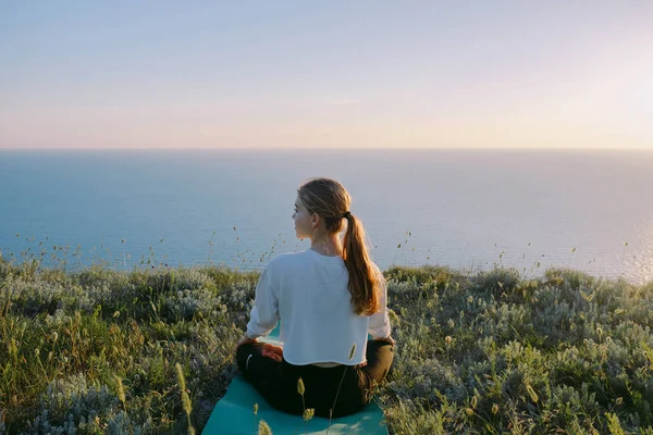 Genç kadın pratik Yoga yılında Lotus pozisyonu açık. genç kız deniz yakınlarındaki tepe üzerinde rahatlatıcı. Sakin, meditasyon, koşu, kavramını eğitim, sakin ol, sağlıklı yaşam ve sağlık. arka görünüm