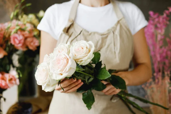 woman florist standing with bouquet of   pink roses indoor in flower shop. Entrepreneurship, small business, workplace concept