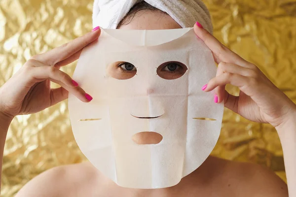 Giovane Donna Applicare Maschera Facciale Tessuto Cosmetico Sfondo Dorato Maschera — Foto Stock
