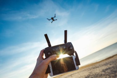 Mavi gökyüzü deniz ve plaj ve el holding denetleyicisi ile smartphone üzerinde uçan robot