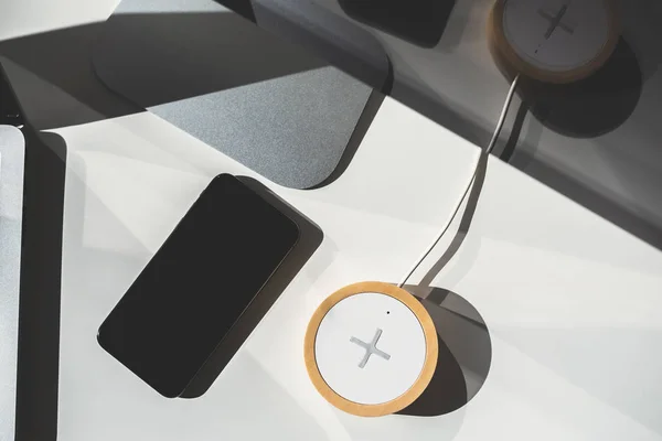 Мобильный телефон и беспроводное зарядное устройство на рабочем столе — стоковое фото