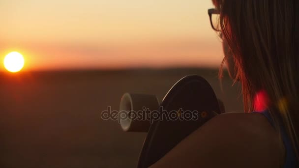 Menina segurando skate e olhando para o pôr do sol — Vídeo de Stock