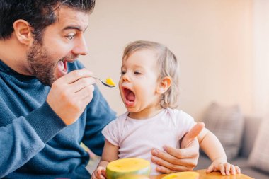 yakın çekim bir genç Baba sevimli küçük kız evde taze mango ile besleme 