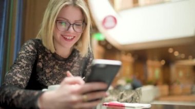 Alışveriş merkezinde akıllı telefon kullanan gözlüklü sarışın genç bir kadın.