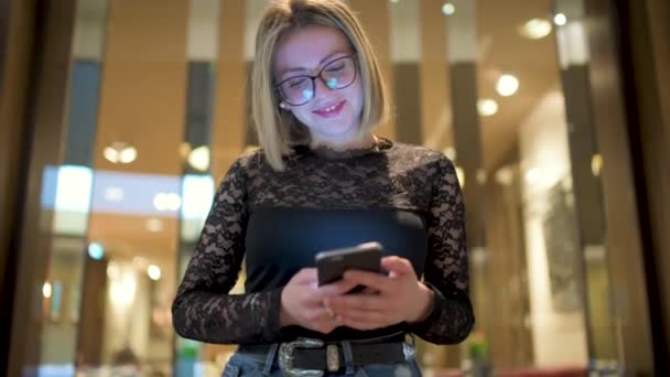 Wanita Muda Berambut Pirang Dengan Kacamata Menggunakan Smartphone Pusat Perbelanjaan — Stok Video