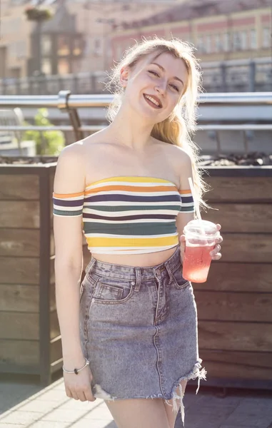 güzel genç gülümsemek kız bir semt güneşli bir günde cadde üzerinde serinletici meyve kokteyli kısa etekli buzlu içecekler