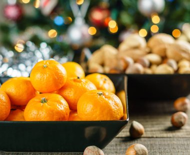 Mandalina ve bir Noel ağacı yakınındaki rustik masada bir kase fındık.