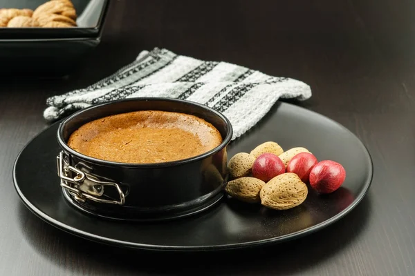 Домашний шоколадный чизкейк в маленькой сковороде на черной тарелке с орехами на столе . — стоковое фото