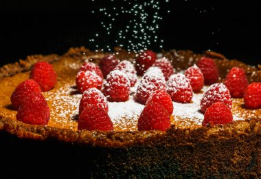 Ahududu ile pudra şekeri bir kar gibi siyah tabloda ile ev yapımı çikolatalı cheesecake.