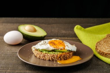 avokado ve yeşil mutfak havlu bir rustik ahşap ve tablo ekmek üzerinde kahverengi bir tabak kızarmış yumurta sandviç.