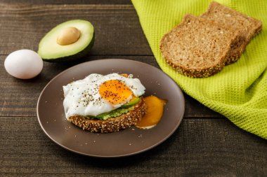 avokado ve yeşil mutfak havlu bir rustik ahşap ve tablo ekmek üzerinde kahverengi bir tabak kızarmış yumurta sandviç.
