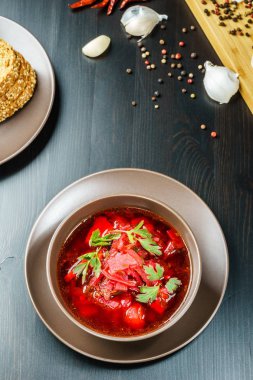 Kırmızı pancar çorbası çorba kahverengi kase üst görünümünde, siyah masa maydanoz ile.