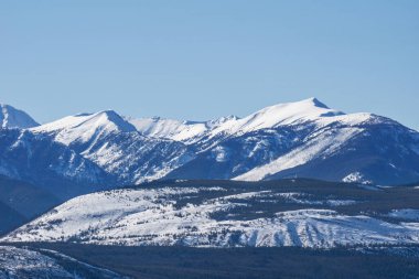 Dağların tepesi, ağaçlar ve karla kaplı güneşli bir bahar günü.