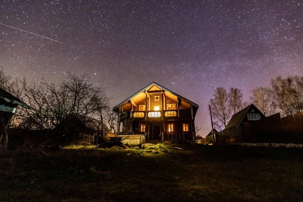 Bahçede kalan ahşap ev. Etrafta ağaçlar var, arka planda yıldızları ve kayan bir yıldızı görebilirsiniz.. 