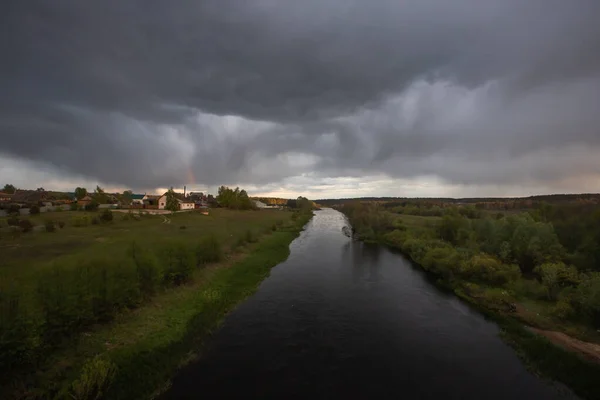 Bu fotoğrafta, çerçevenin büyük bir kısmı fırtınalı gökyüzü tarafından nehrin sakin suyuna yansıtılır. Sağda pembe bulutlar ve solda koyu mavi bulutlar. Sol tarafta yoğun bir orman yetişiyor. Gün batımı..