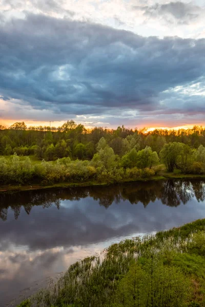 Bu fotoğrafta, çerçevenin büyük bir kısmı fırtınalı gökyüzü tarafından nehrin sakin suyuna yansıtılır. Sağda pembe bulutlar ve solda koyu mavi bulutlar. Sol tarafta yoğun bir orman yetişiyor. Gün batımı..