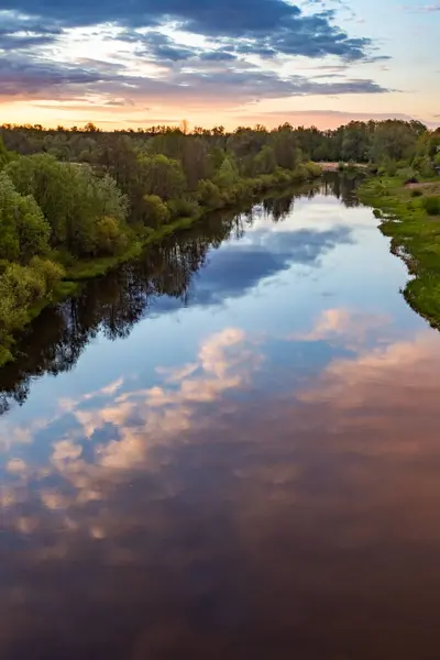 Bu fotoğrafta, çerçevenin büyük bir kısmı fırtınalı gökyüzü tarafından nehrin sakin suyuna yansıtılır. Sağda pembe bulutlar ve solda koyu mavi bulutlar. Sol tarafta yoğun bir orman yetişiyor. Gün batımı..