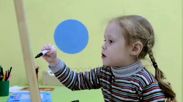 Auf der Tafel zeichnet ein kleines Mädchen mit einem Filzstift eine Form — Stockvideo
