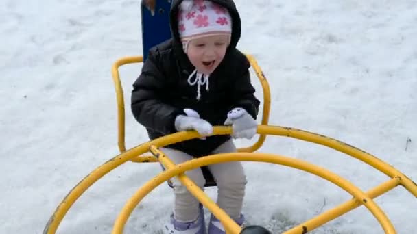 Nettes kleines Mädchen schaukelt bei kaltem Schneetag im Winter auf Spielplatz — Stockvideo