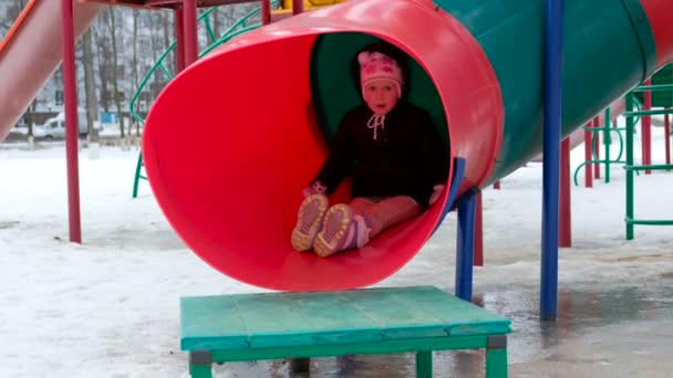 Mignonne petite fille balançant sur aire de jeux à froid journée enneigée en hiver — Video