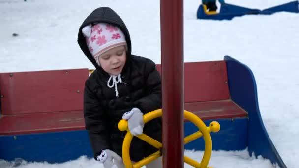 Carina bambina che oscilla sul parco giochi nella fredda giornata innevata in inverno — Video Stock